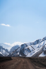 A rough dirt road or track leading forward into a deep valley surrounded by high, steep mountains covered in patches of white snow