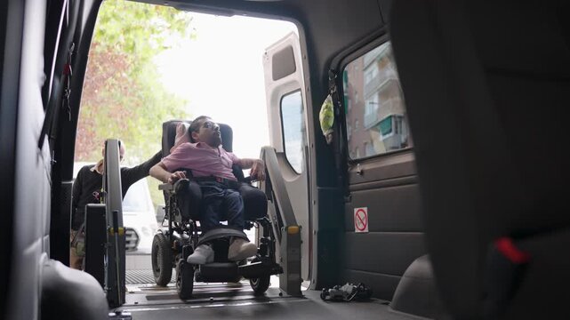 Man with a disability using an accessible van with a wheelchair lift for transport. A caregiver assists him onto the vehicle platform