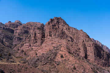 A massive, rugged, reddish-brown mountain peak rising steeply against a clear, vibrant blue sky on a bright day