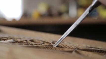 Close-up of an artisan's hand using a chisel to carve intricate floral ornaments into a wooden board, showcasing traditional woodworking skills and precise attention to beautiful artistic details.

