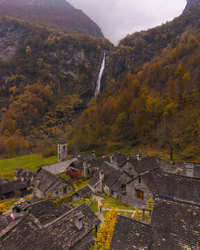 Aerial view of the rustic village nestled amongst the warm autumn colors, with a dramatic waterfall cascading in the background, Foroglio, Ticino, Switzerland.