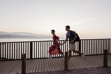 Happy couple running along wooden boardwalk at sunset