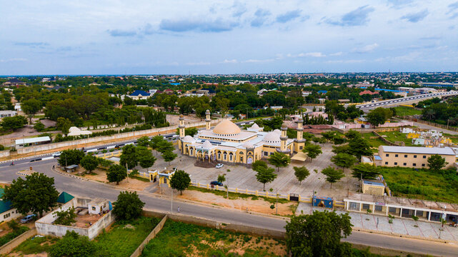 Aerial view of a grand mosque bathed in soft sunlight, its golden dome and minarets rising above the lush greenery, Banu Coomassie, Katsina, Nigeria.