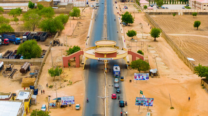 Aerial view of the dusty IBB Way, with its distinctive arched gateway, cutting through the arid landscape amidst scattered greenery, Katsina, Katsina, Nigeria.