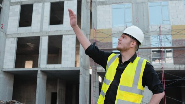 A construction worker is pointing upwards with his hand at a construction site
