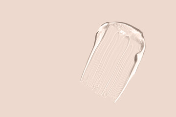 Squeezed cosmetic clear cream gel texture isolated on beige background. Close up transparent serum drop smear