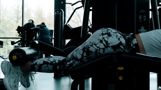 The woman is performing a lying leg curl exercise on a fitness machine