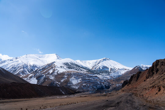 Wide panoramic view of a vast landscape featuring snow-capped mountains and a large, visible open-pit mine site on the lower slopes