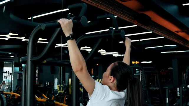 The woman is performing pull-ups on a pull-up bar in a gym