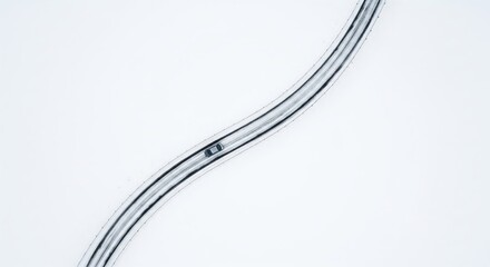 Aerial View of a Curved Snowy Road with a Single Vehicle Traveling Through Winter Landscape