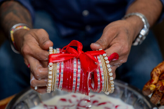 Hands holding red and white bangles with a red ribbon, a cultural tradition