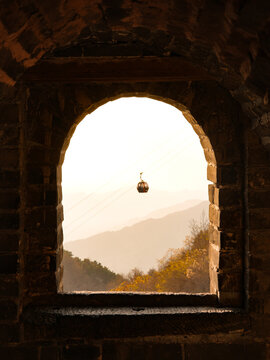 View of a cable car suspended in the distance, framed by an ancient stone archway and rolling hills bathed in soft light, Beijing, Beijing, China.
