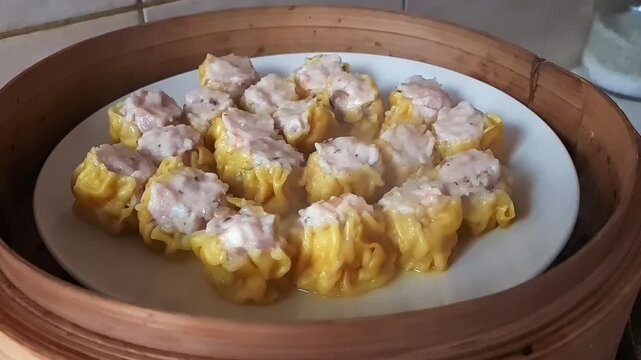 A plate full of steaming hot sui mai dim sum dumplings in a bamboo steamer.