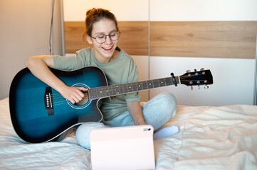 A teenage girl plays the guitar, showing it to someone online while smiling, illustrating joy of music, digital interaction, and engaging leisure activities at home