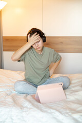 A teenage girl sits on her bed in home clothes, holding her head and looking upset, showing emotional distress, stress, and everyday teenage struggles in a cozy home environment