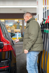 A young man opens a car&rsquo;s fuel tank flap at a gas station, preparing to refuel, showing everyday refueling, human interaction with vehicles, and the development of urban infrastructure