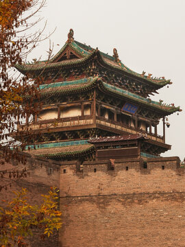 View of ancient architecture with its layered roof and brick walls contrasting with the muted sky, framed by foliage, Jinzhong, Shanxi, China.