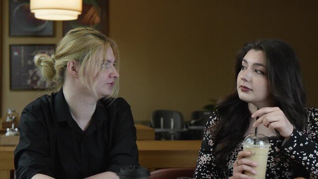 woman on the right is stirring her drink with a straw while the woman on the lef