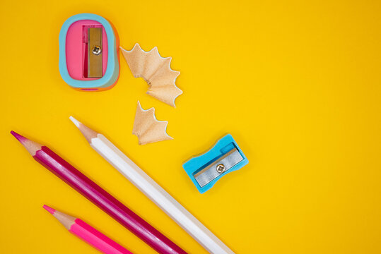 Top view of colorful pencils, a dual-hole pencil sharpener and shavings arranged on a bright yellow background. Back-to-school and education stationery concept. 