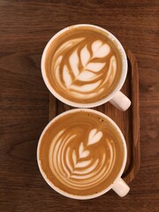 Two cappuccino coffee cups with the heart shape closeup top view, rustic wooden background