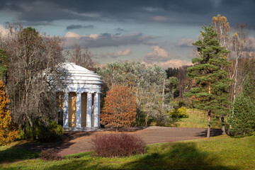 Temple of Friendship pavilion, designed as a rotunda decorated with 16 white Doric columns, bas-relief medallions, and light stucco molding, in Pavlovsk City Park on a sunny autumn day.