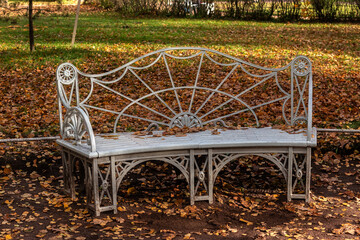 Solid iron bench with a wrought iron backrest and base, painted silver, in an autumn city park.