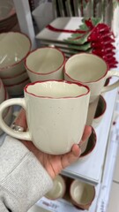 Christmas-themed ceramic mugs with red rims held in a store setting