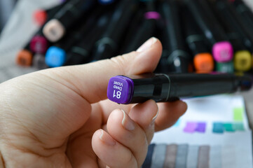 Alcohol-based marker with chisel tip held above color swatches. Ideal for illustrating art supplies, creative tools, drawing materials, and product reviews.