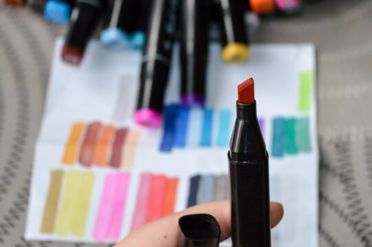 Alcohol-based marker with chisel tip held above color swatches. Ideal for illustrating art supplies, creative tools, drawing materials, and product reviews.