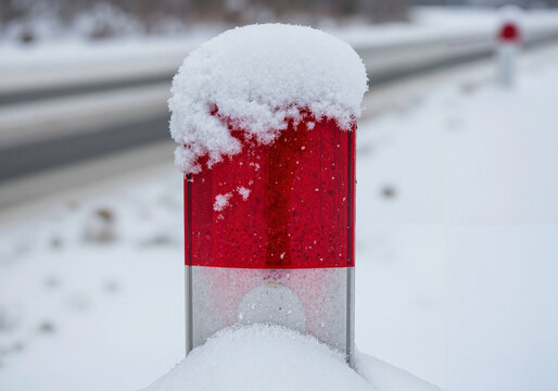 Snow-covered road marker with red reflectors in winter landscape  