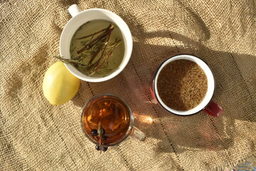 A cup of green tea with lemon and rosemary on burlap, top view