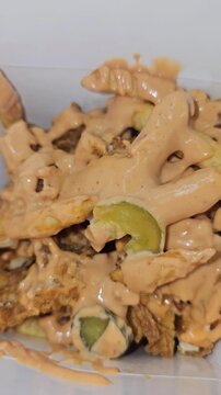 Savory dish featuring chopped loaded chicken french fries, and pickles generously smothered in a creamy, tangy, thousand-island-style sauce, served in a container.