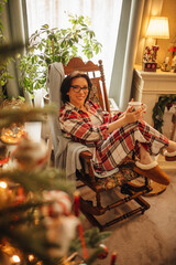 A woman in a checkered pyjama is drinking tea in a Christmas interior