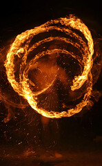 Spirale de flammes et d'&eacute;tincelles cr&eacute;&eacute;e par un jongleur de feu en mouvement sur fond noir, prise de vue nocturne