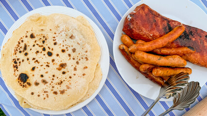 Golden crepes mingle with sizzling sausages on a striped tablecloth, evoking Pancake Day festivities and rustic brunch gatherings