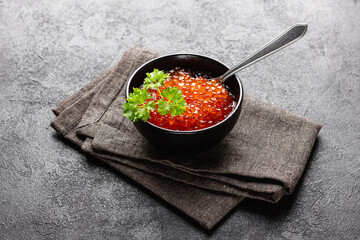 Red caviar in black bowl with parsley on dark table