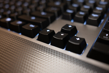 Close-up of arrow keys on a black gaming keyboard with blue LED backlighting. The shallow depth of field and textured surface create a high-tech, modern feel.