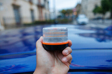 Hand placing a v16 emergency beacon light on a car roof, signaling roadside safety