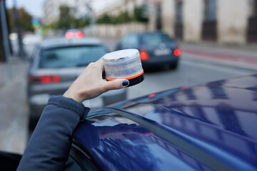 Hand placing a v16 emergency beacon light on a car roof, signaling roadside safety
