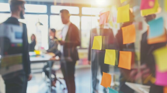A group of diverse professionals engaged in a brainstorming session. Colorful sticky notes are visible on a glass wall. The atmosphere is collaborative and creative.