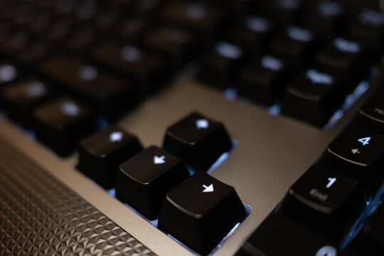 Close-up of arrow keys and numpad on a modern black keyboard. Blue backlighting and a textured surface create a high-tech, gaming aesthetic.