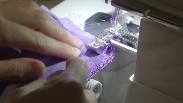 Sewing purple fabric edge on a serger machine in home studio during the afternoon