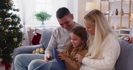 Christmas family reading book together at home. Parents and daughter sit by the tree, sharing cozy holiday stories with their child. Warm portrait of family bonding and festive tradition. - Powered by Adobe