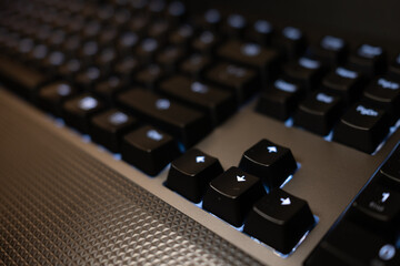 Close-up of a modern black gaming keyboard with blue LED backlighting. The shallow depth of field creates a high-tech, futuristic background for technology concepts.