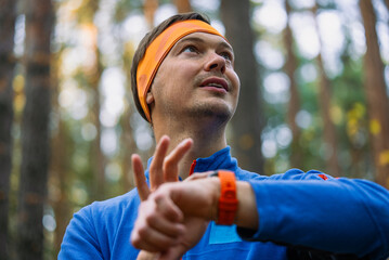 Naklejka premium Young male runner in sportswear checks his smartwatch while training outdoors in a city park amid autumn trees, focused on tracking fitness progress and endurance data