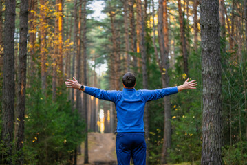 Man stretching during a fitness workout in a park, reaching out with open arms, finding comfort and healthy living in the serene forest environment, connecting with the peaceful nature