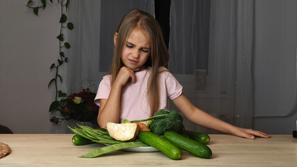 Young girl with long hair, wearing a pink shirt, is looking skeptically at a plate of fresh vegetables, expressing a humorous reaction to healthy eating choices