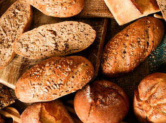 Close-up of freshly baked homemade wheat and rye rolls. In the background, various types of bread with sesame, sunflower and flaxseed seeds. Traditional bread from a Polish bakery.