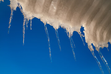 Icicles are melting and dripping water against a vibrant blue sky, creating a beautiful contrast between the cold ice and the warm sunlight