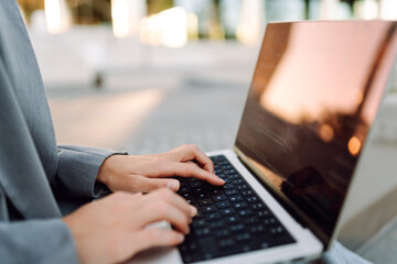 Close-up of a woman's hands typing on a laptop outdoors. A businesswoman enjoys the sunset and her remote work. Conceptual image of freelancing, business, and technology.